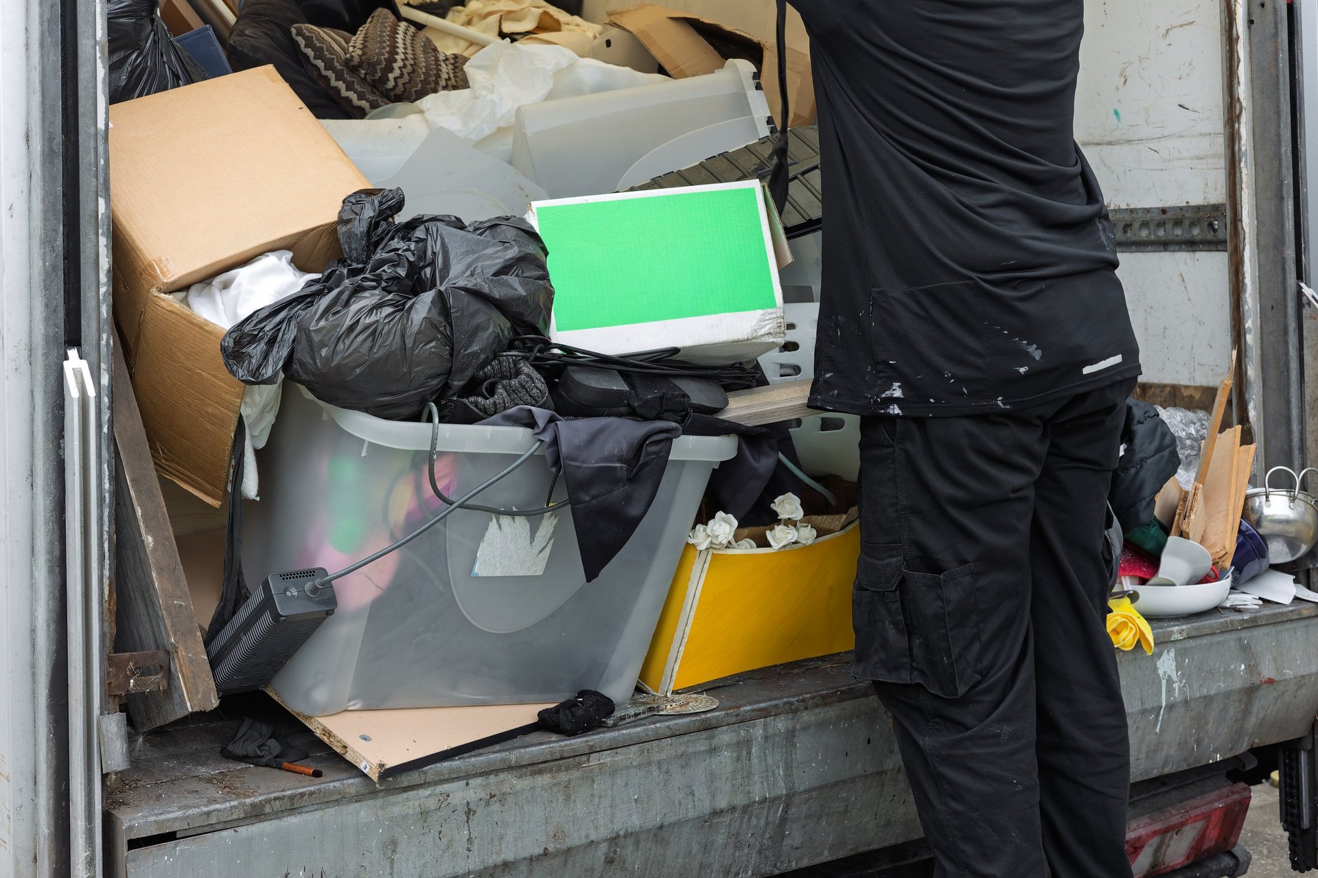 Worker unloading mixed waste, household items, and rubbish from junk removal truck
